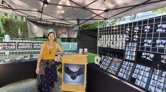 Woman standing next to a checkout booth within an outdoor booth with jewelry displays at a art market