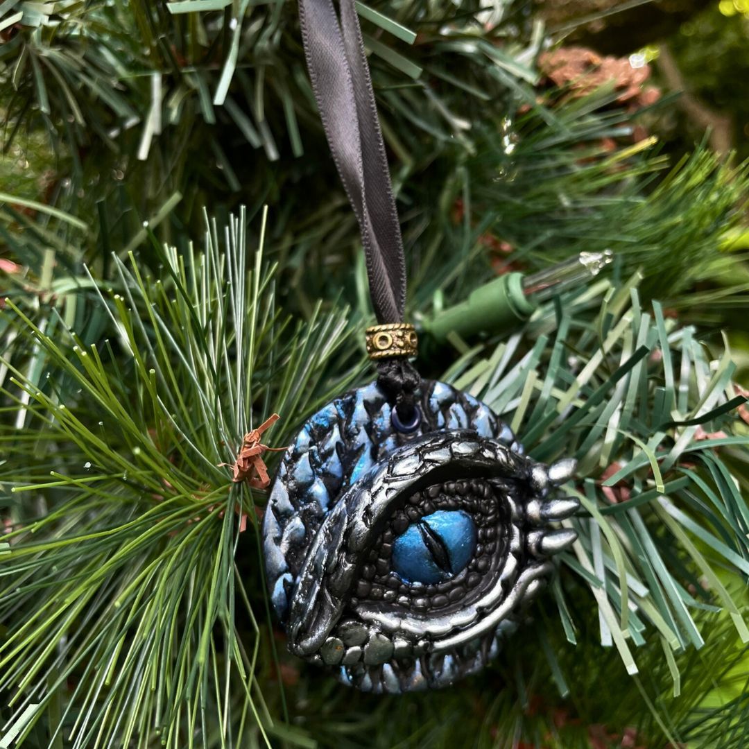 A round dragon eye ornament with metallic silver and blue coloring with black satin ribbon hanging on a Christmas tree.