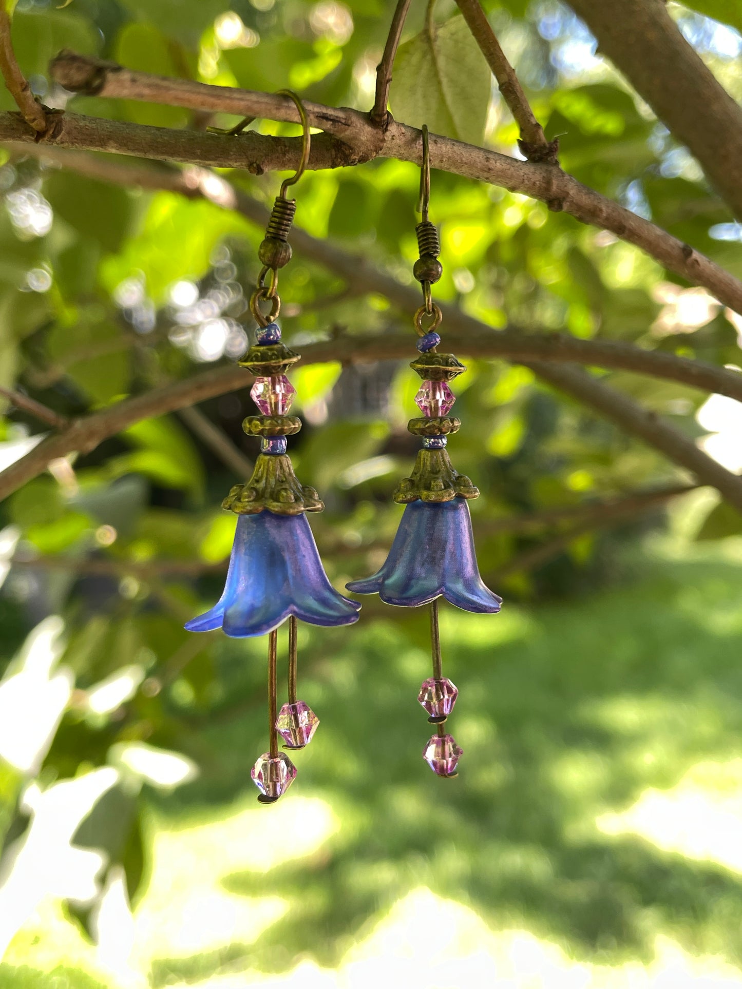 Blue flower dangle earring with antique bronze and purple beads on a branch in a garden.