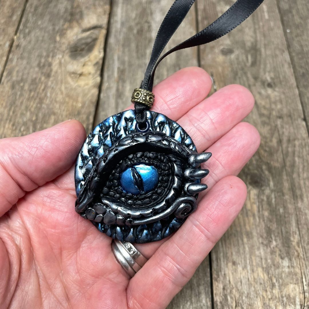A round dragon eye ornament with metallic silver and blue coloring with black satin ribbon held in a hand