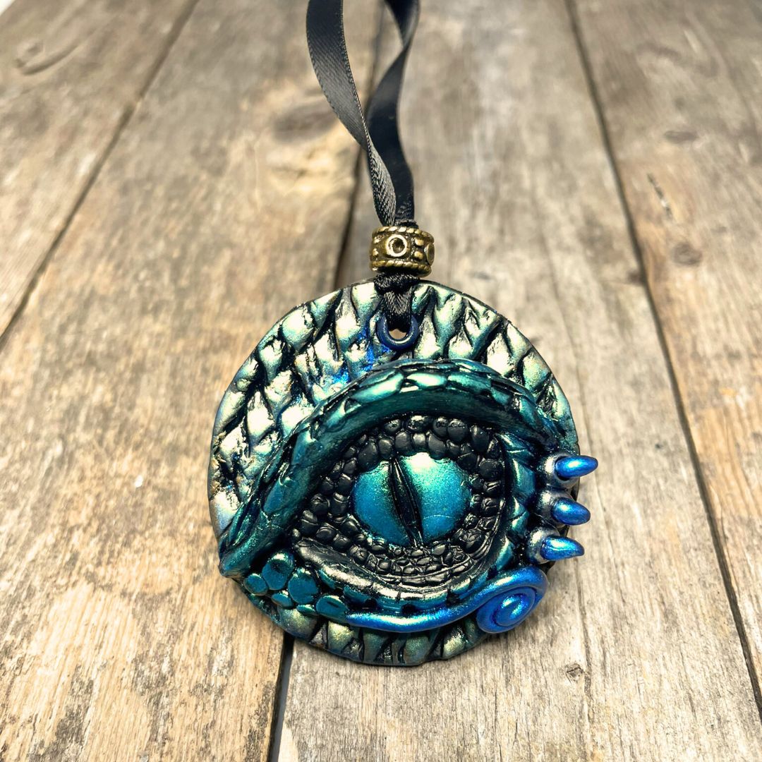 A round dragon eye ornament with metallic green gold and blue coloring with black satin ribbon