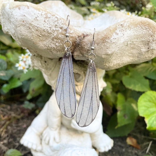 Light gray Sparly dragonflly dangle earrings hanging from a garden ornament.