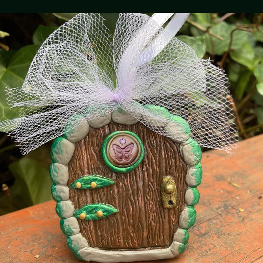 A small arched fairy door ornament with butterfly and leaf details with a pink tule bow in a garden.