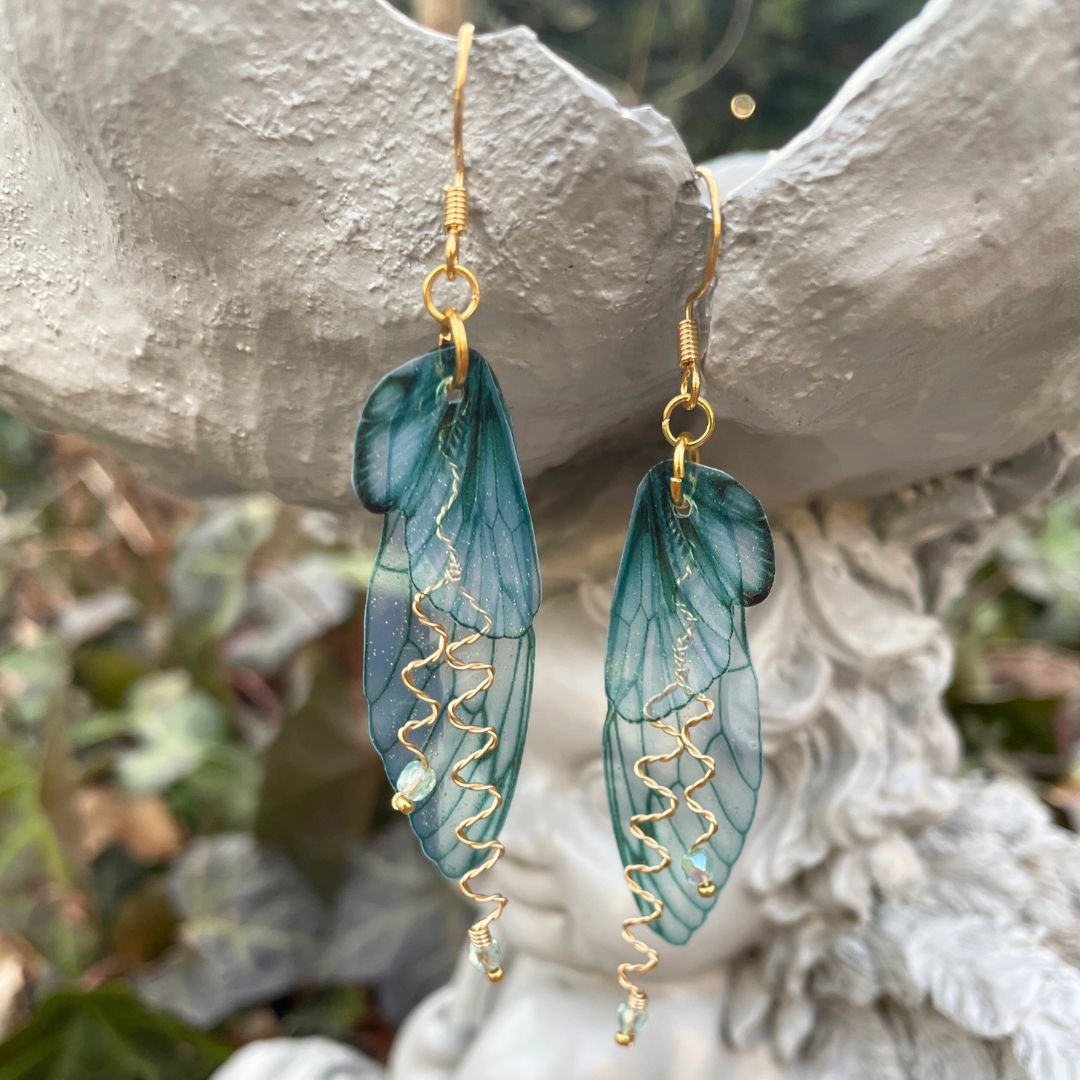Forest fairy earrings with gold wires against a garden ornament