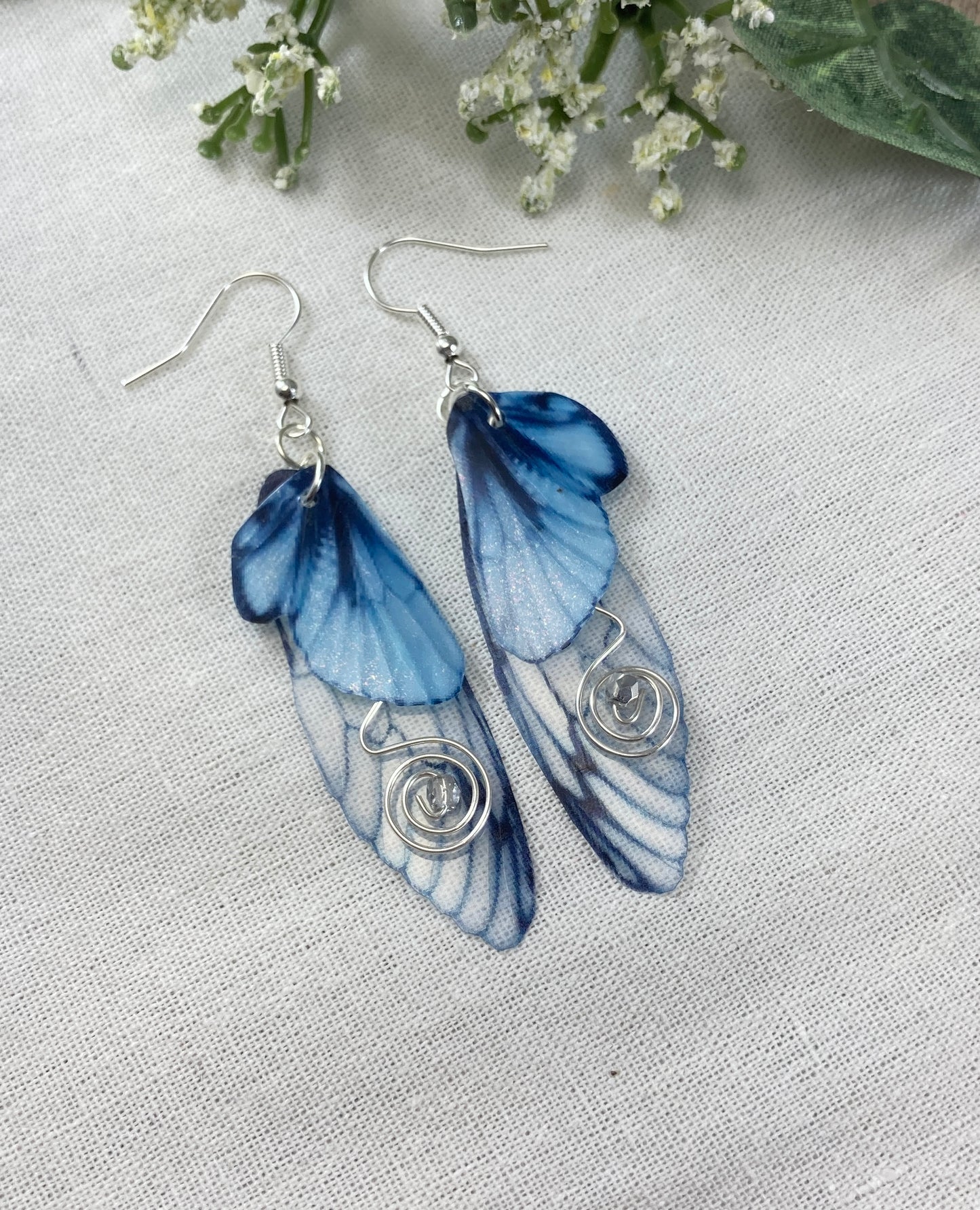 blue butterfly clip earrings flat lay on a canvas pouch with flowers