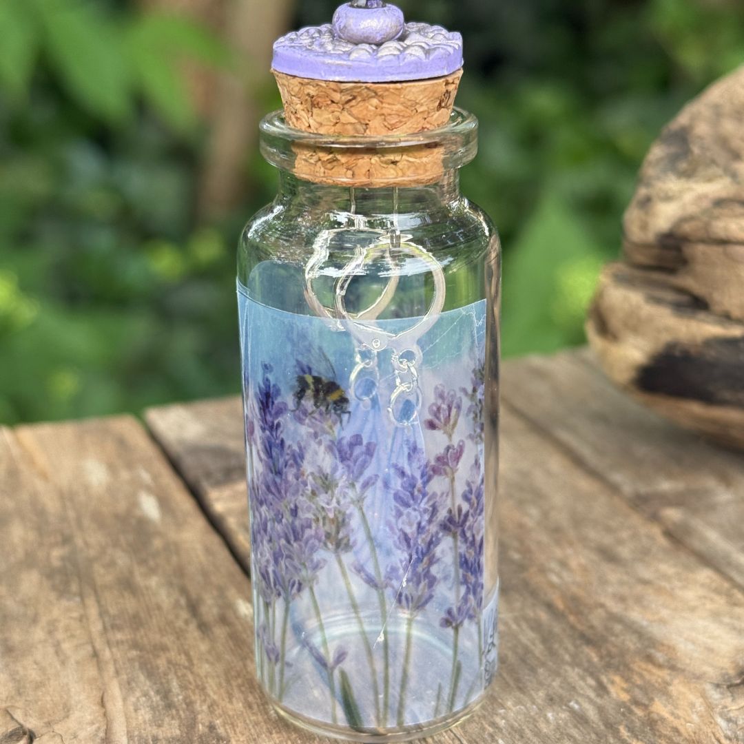 Glass bottle with cork lid featuring a lavender design on a wooden surface with a blurred natural background