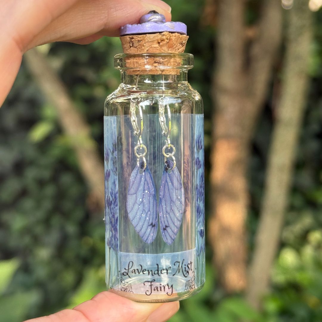 Bottle of 'Lavender Mist Fairy' earrings held by a hand with a natural background