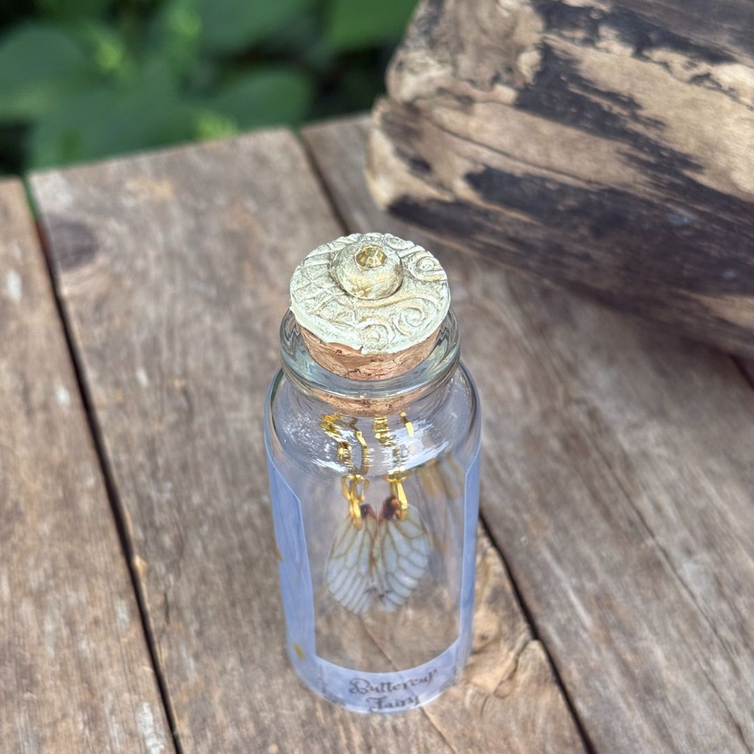 Small glass bottle with with fairy earrings inside a decorative cork lid on a wooden surface