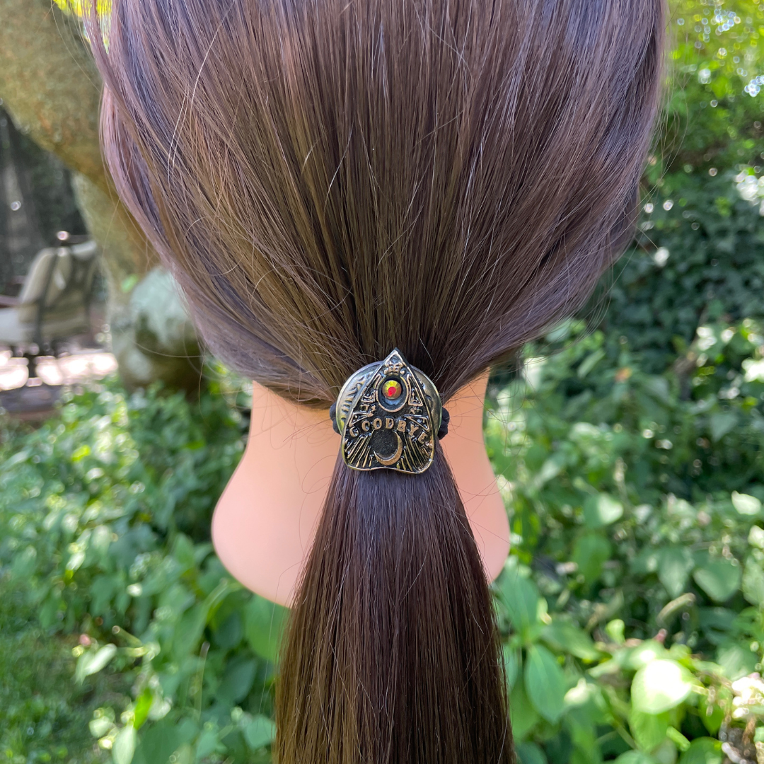 Ouija board planchette hair tie with  red crystal and the word 'goodbye' in gold lettering on a model.