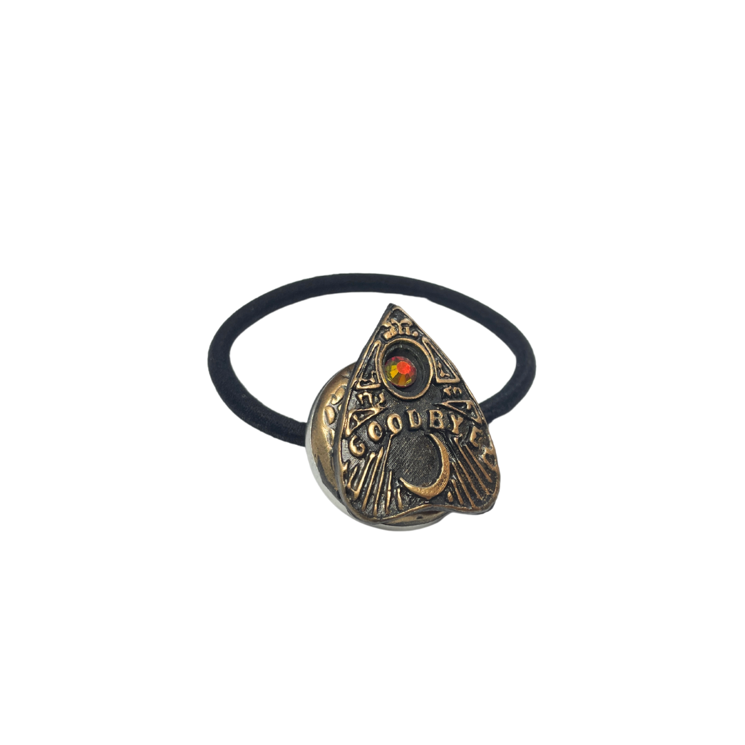 Ouija board planchette hair tie with  red crystal and the word 'goodbye' in gold lettering on a white background