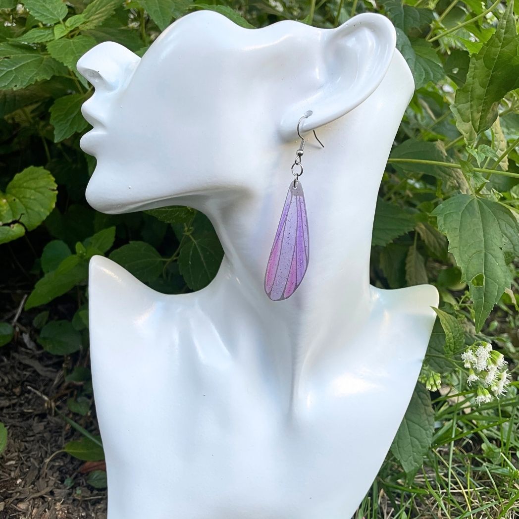 blue and gray sparkly long dangle dragonfly earrings dangling from an earring bust.