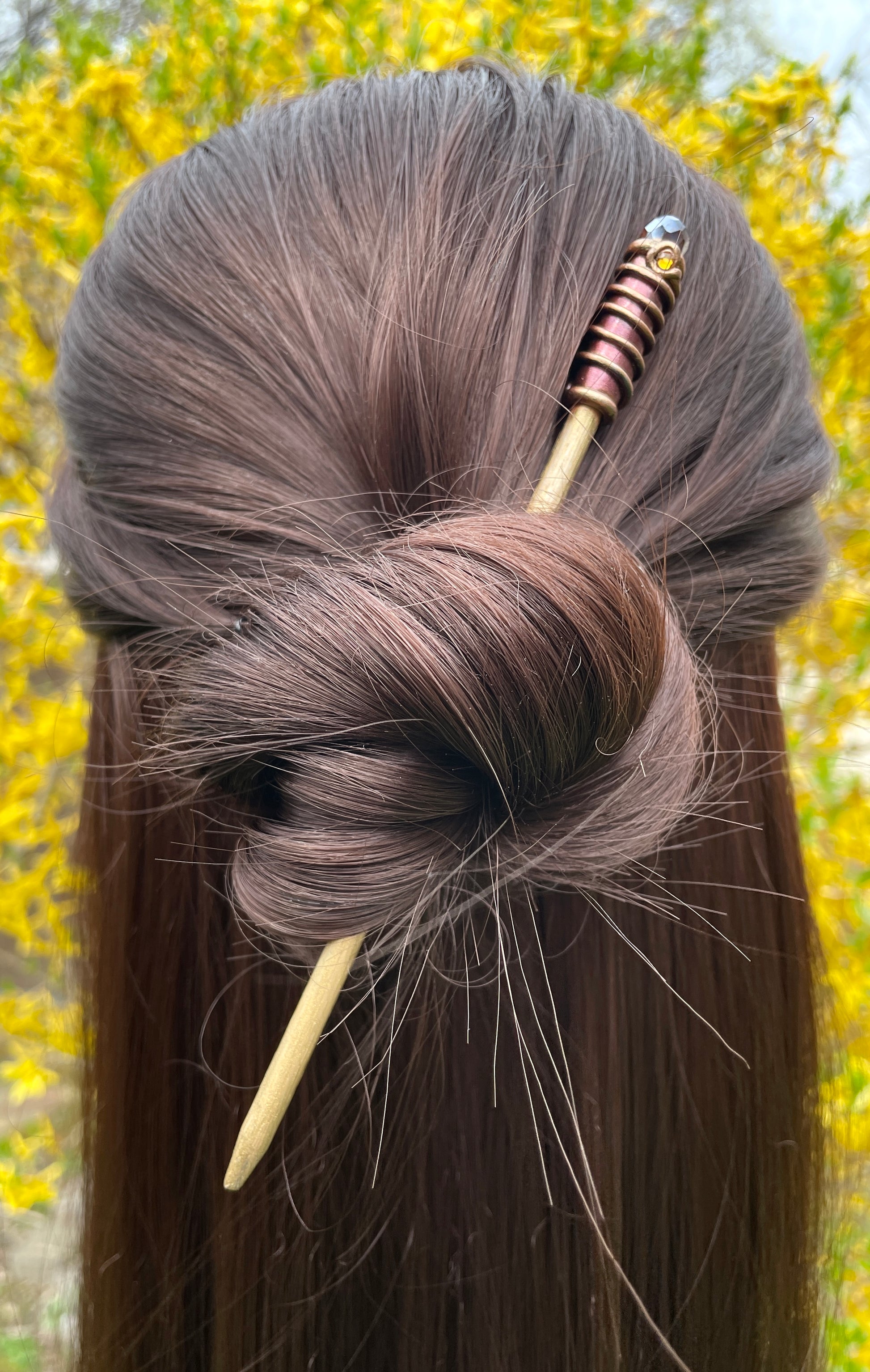 Model wearing gold painted wood hair stick with bronze and gold spiral clay hand painted details with dark AmberAB crystal.
