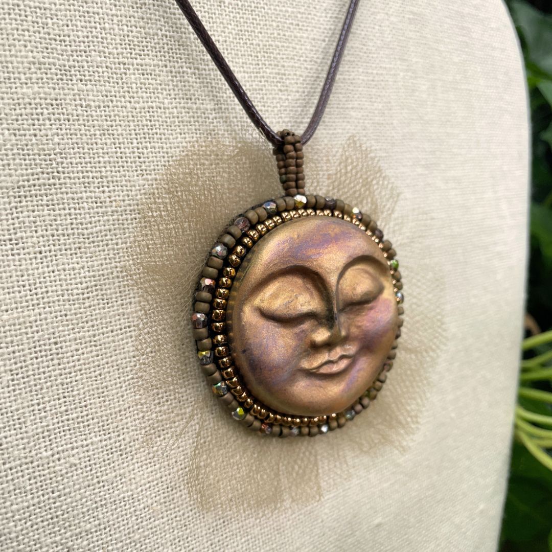 Beaded sun goddess statement pendant with sleeping face and gold beading and tulle around the edge . On a display stand