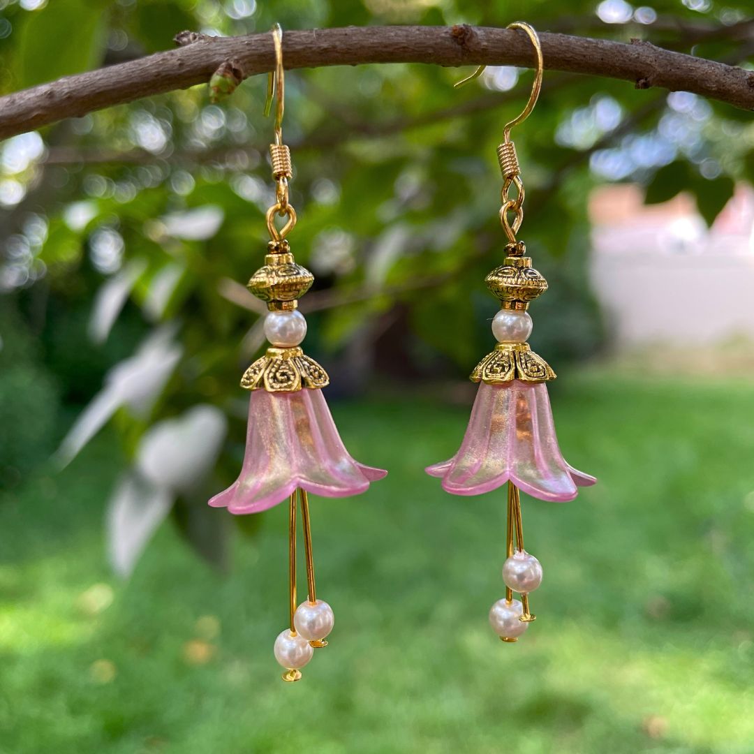 pink bell flower earrings with gold accents and pink pearls. Earrings hanging on a tree branch.