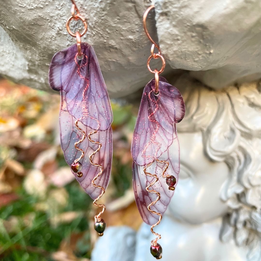 Berry colored fairy wing earrings with crystals hanging from a garden ornament