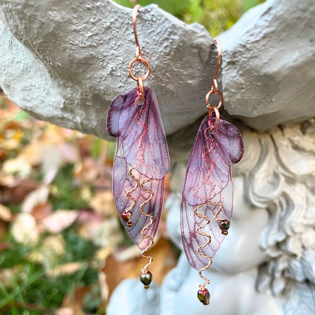 Berry colored fairy wing earrings with crystals hanging from a garden ornament