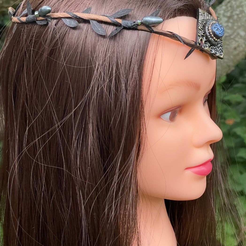 Side profile of blue moon on a golden textured diamond shape focal on a brown wire leaf crown on a model.
