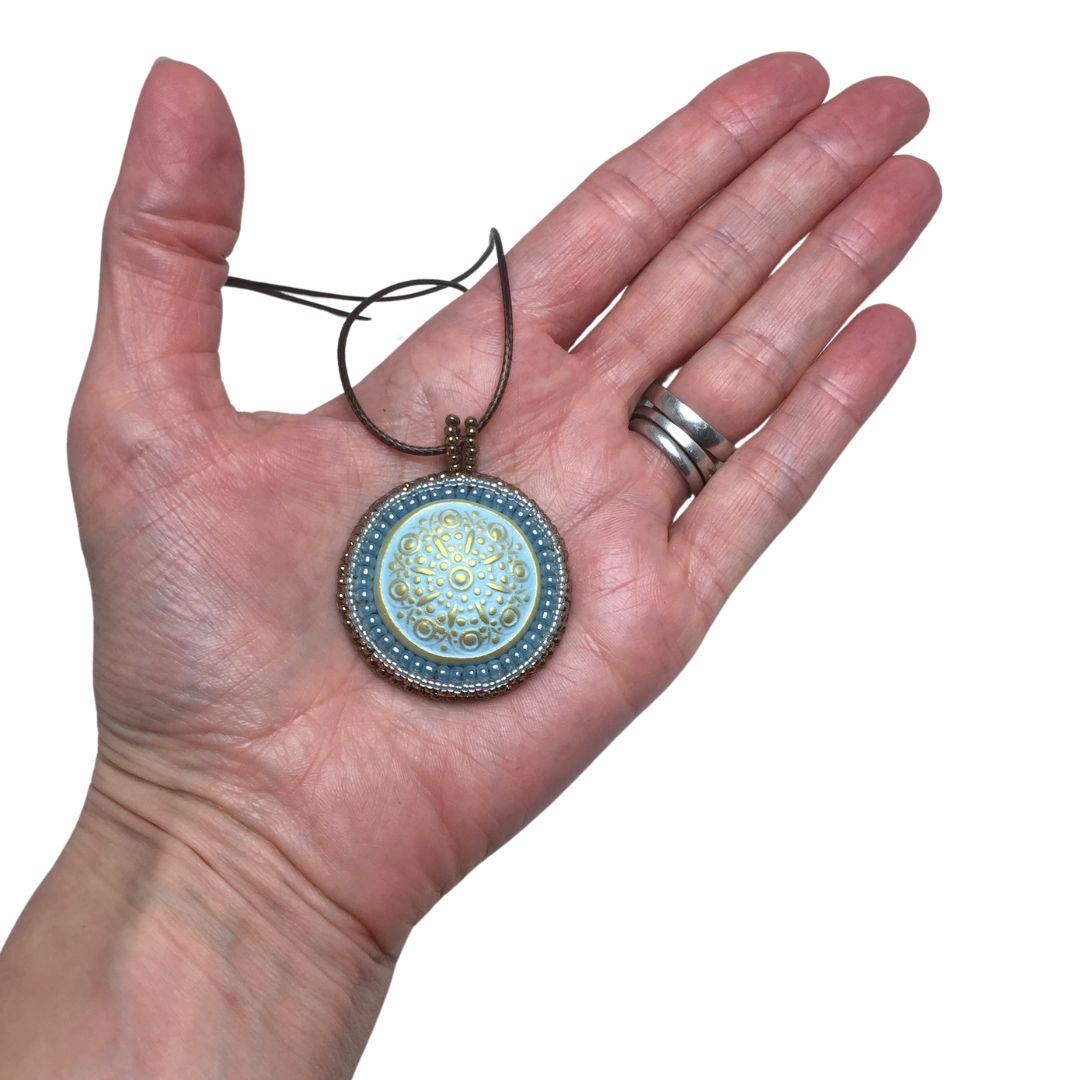 blue floral circle necklace held in a hand against a white background.
