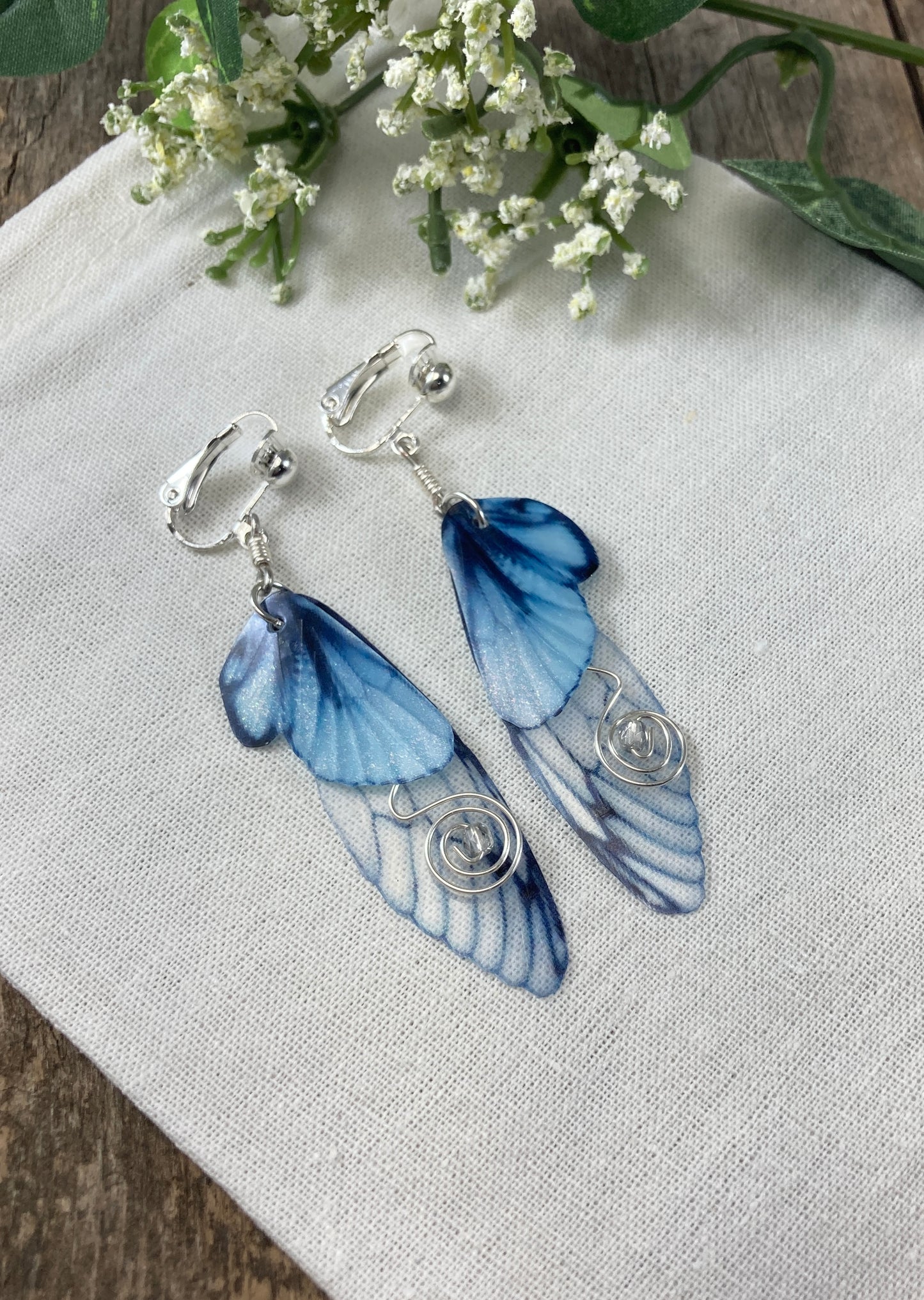 blue butterfly clip earrings flat lay on a canvas pouch with flowers