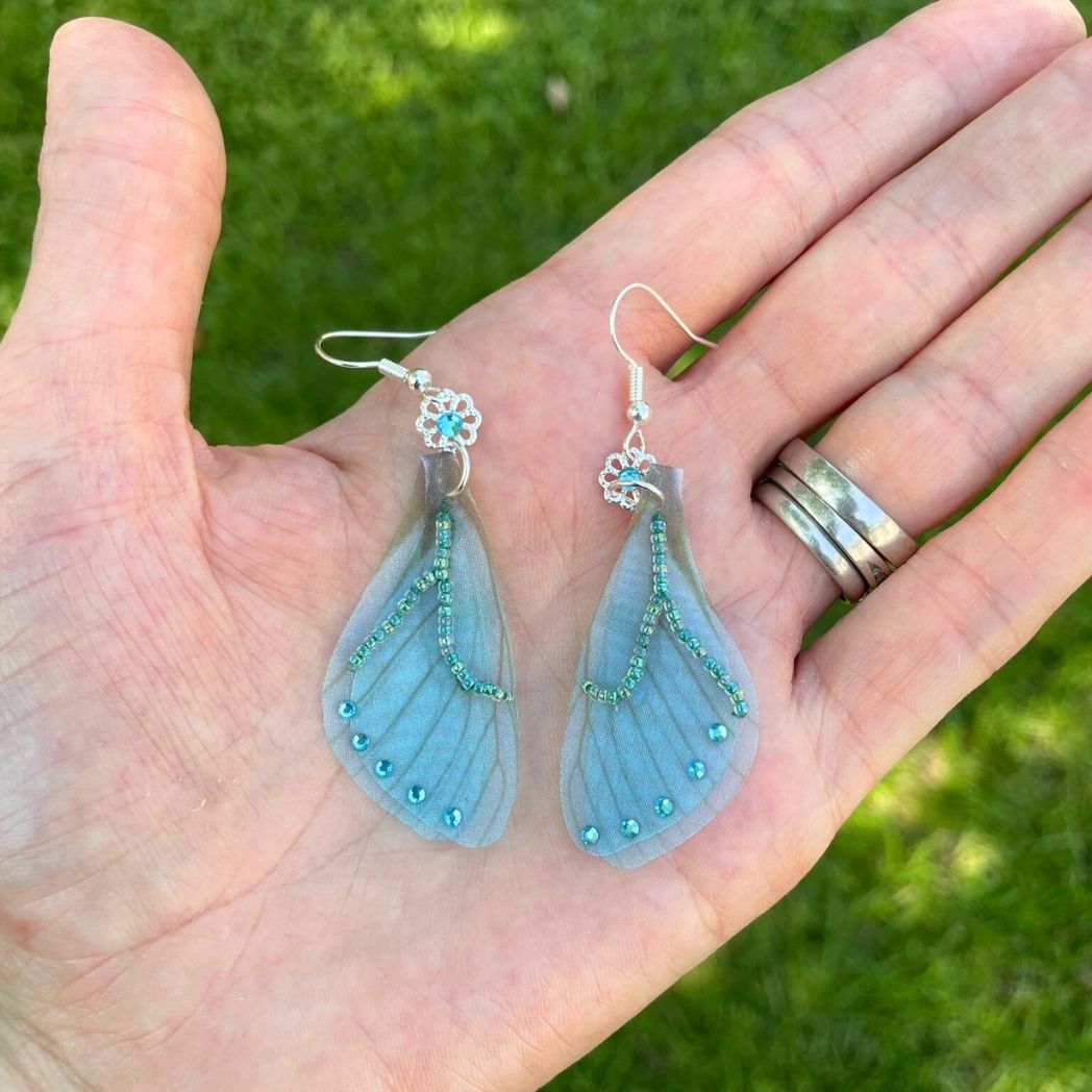 Blue chiffon butterfly wing earrings with silver crystal flower, charm and crystals on the wings in a hand