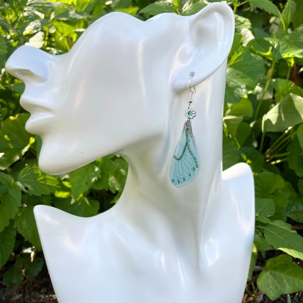 Model wearing blue chiffon butterfly wing earrings with silver crystal flower, charm and crystals on the wings.