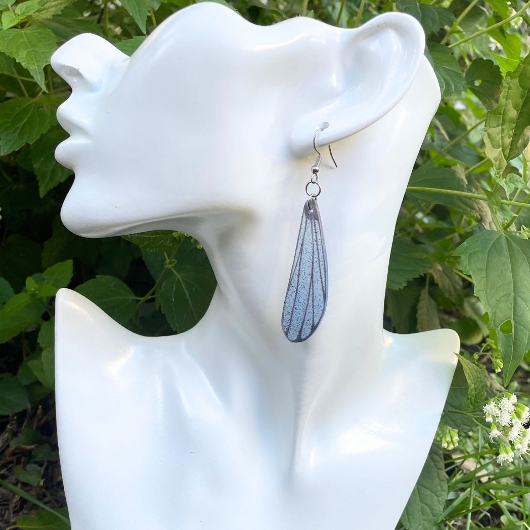 blue and gray sparkly long dangle dragonfly earrings dangling from an earring bust.