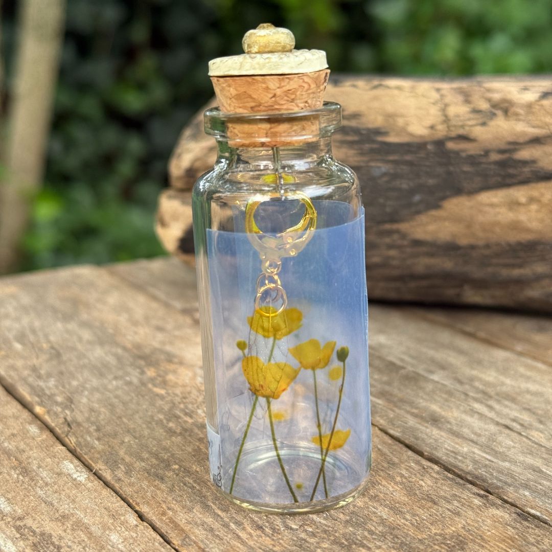 Glass bottle with cork lid containing yellow flowers on a wooden surface