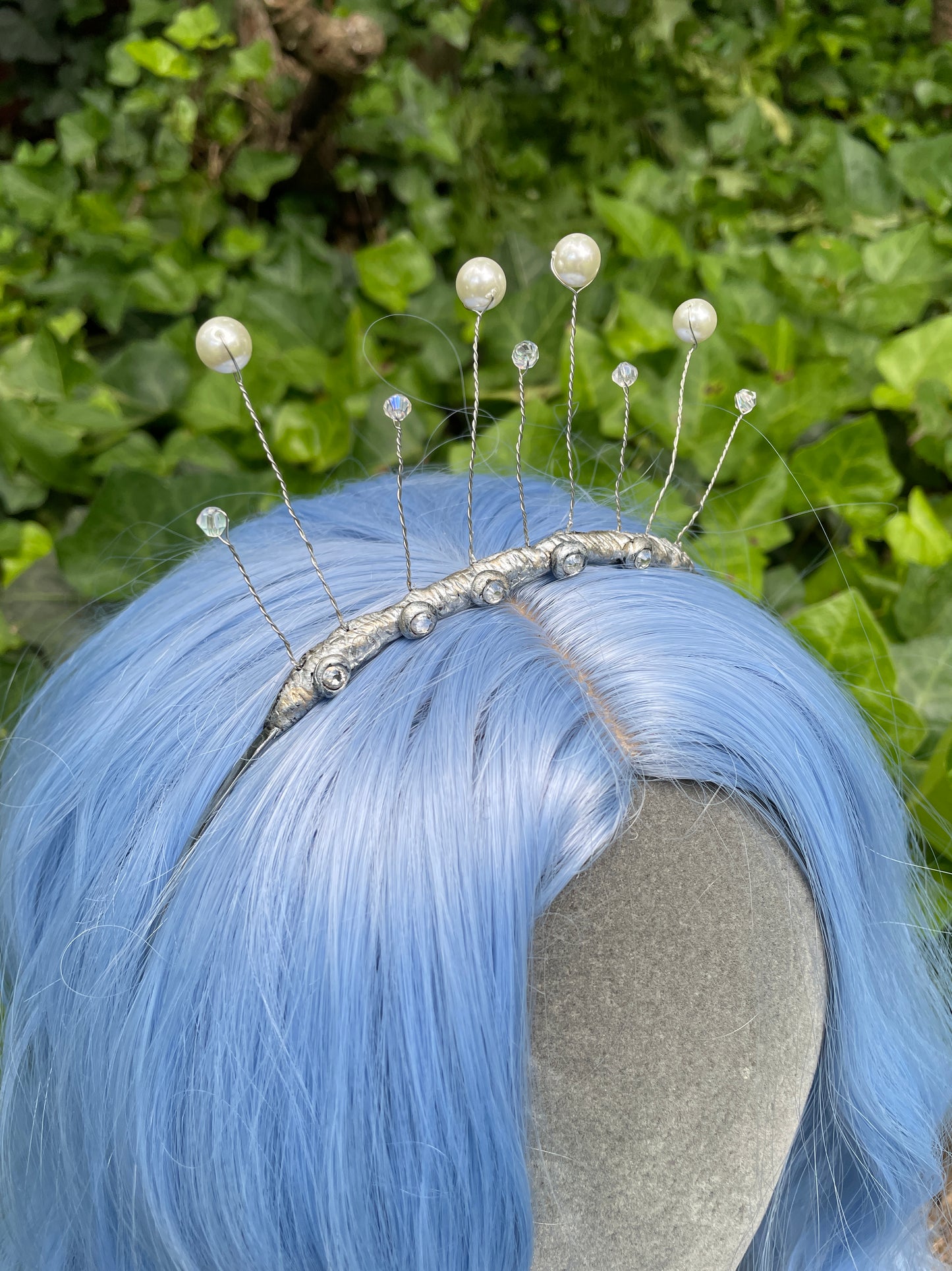 Side profile of a Closeup of celestial tiara on model with blue wig in a garden setting