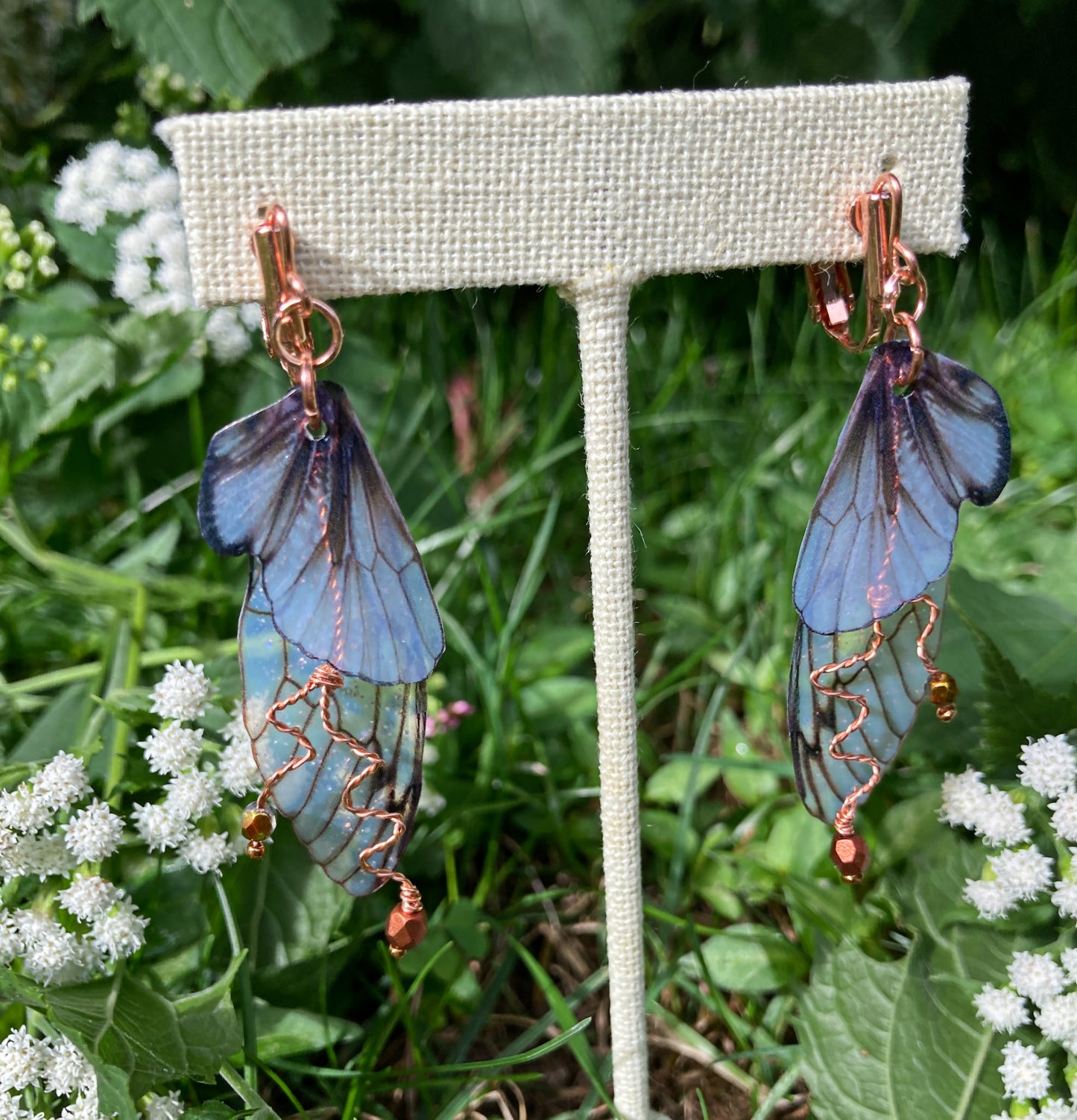 Fairy wing earrings with copper wired crystals with clip on components on an earring stand in garden