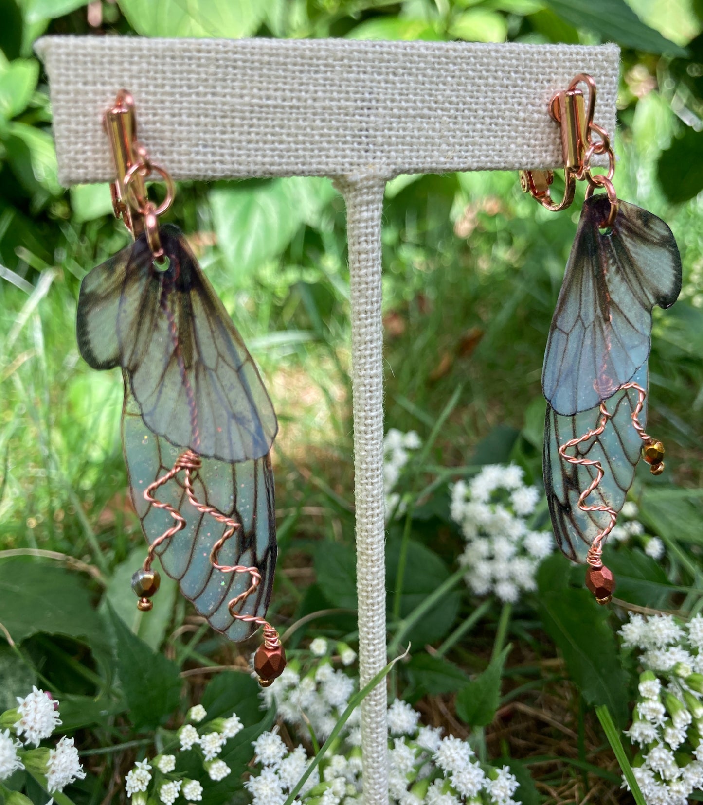Fairy wing earrings with copper wired crystals with clip on components on an earring stand in garden