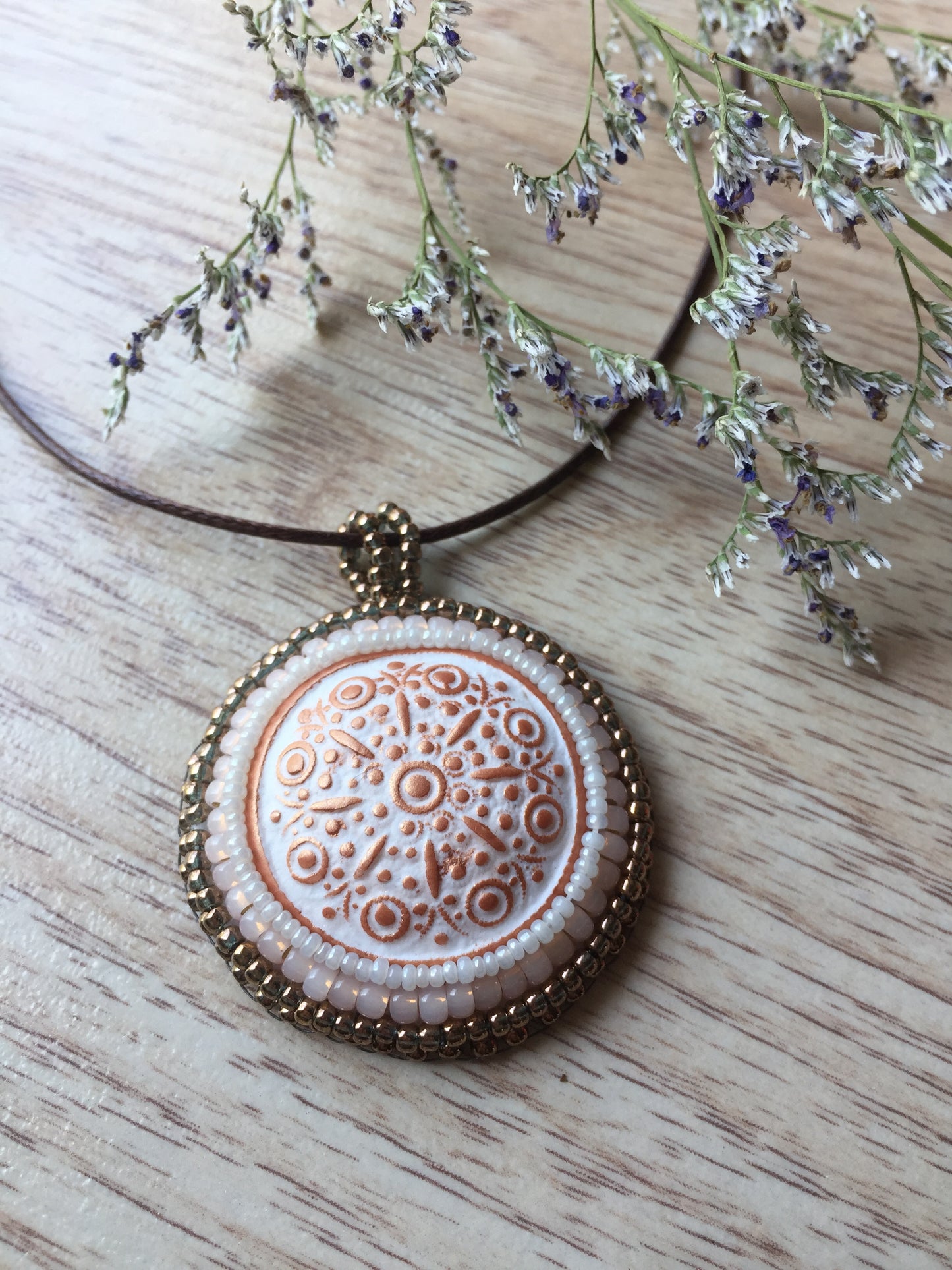 copper floral round pendant on wood surface and flowers to the right corner