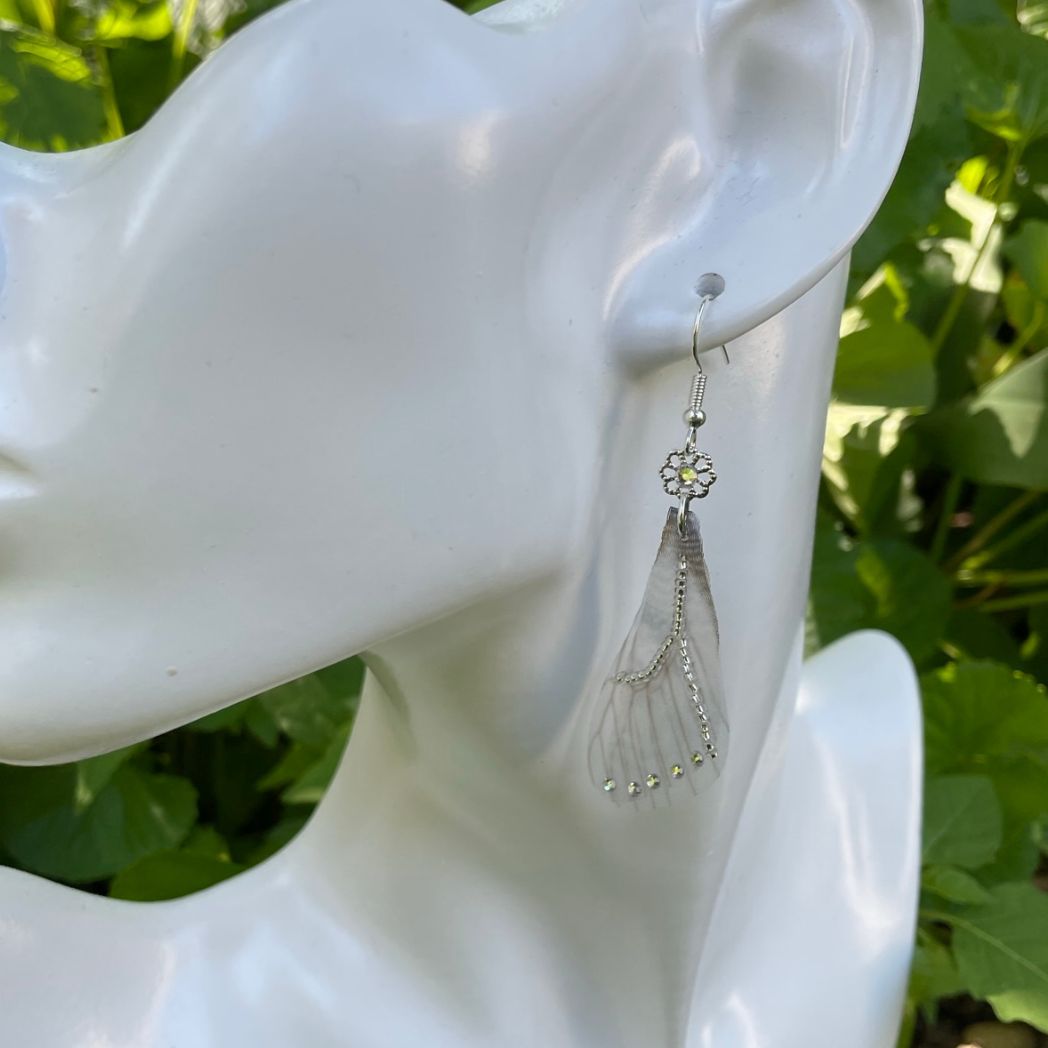 Silver beaded gray sheer fabric butterfly wing earrings with crystals and a flower bead connecting to the ear wires on a model.