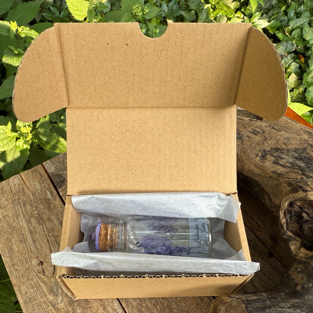 Open cardboard box with a bottle of lavender essential oil on a wooden surface with greenery in the background