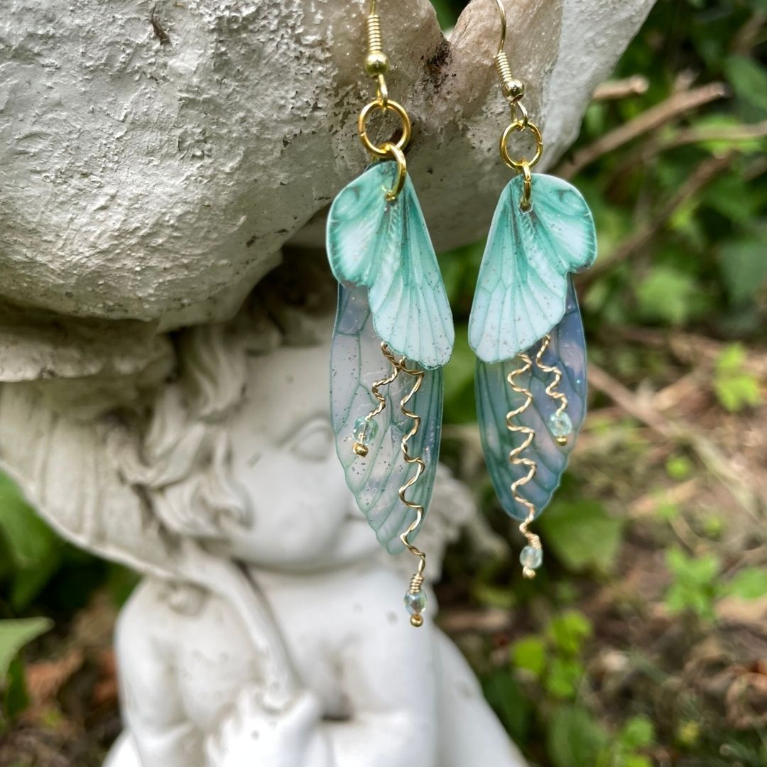 Mint green double wing fairy wings with gold twisted wires with crystals. and gold french ear hooks hanging on a angel garden ornament.