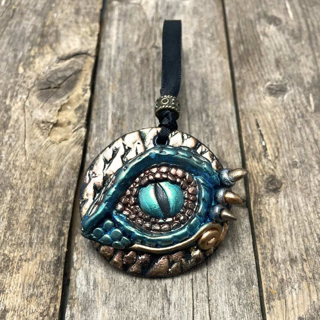 A round dragon eye ornament with metallic green gold and bronze coloring with black satin ribbon