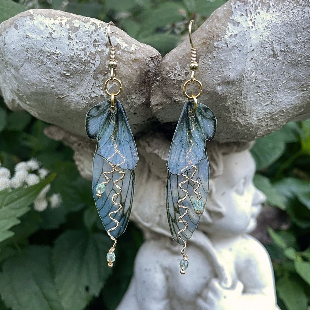 olive green fairy earrings suspended on a garden ornament in a garden setting.