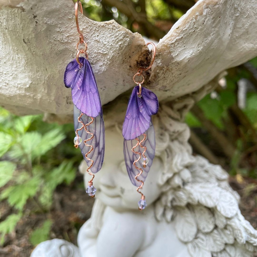 Violet purple fairy wing earrings with lavender crystals and copper wires. Hanging from fairy garden ornament.