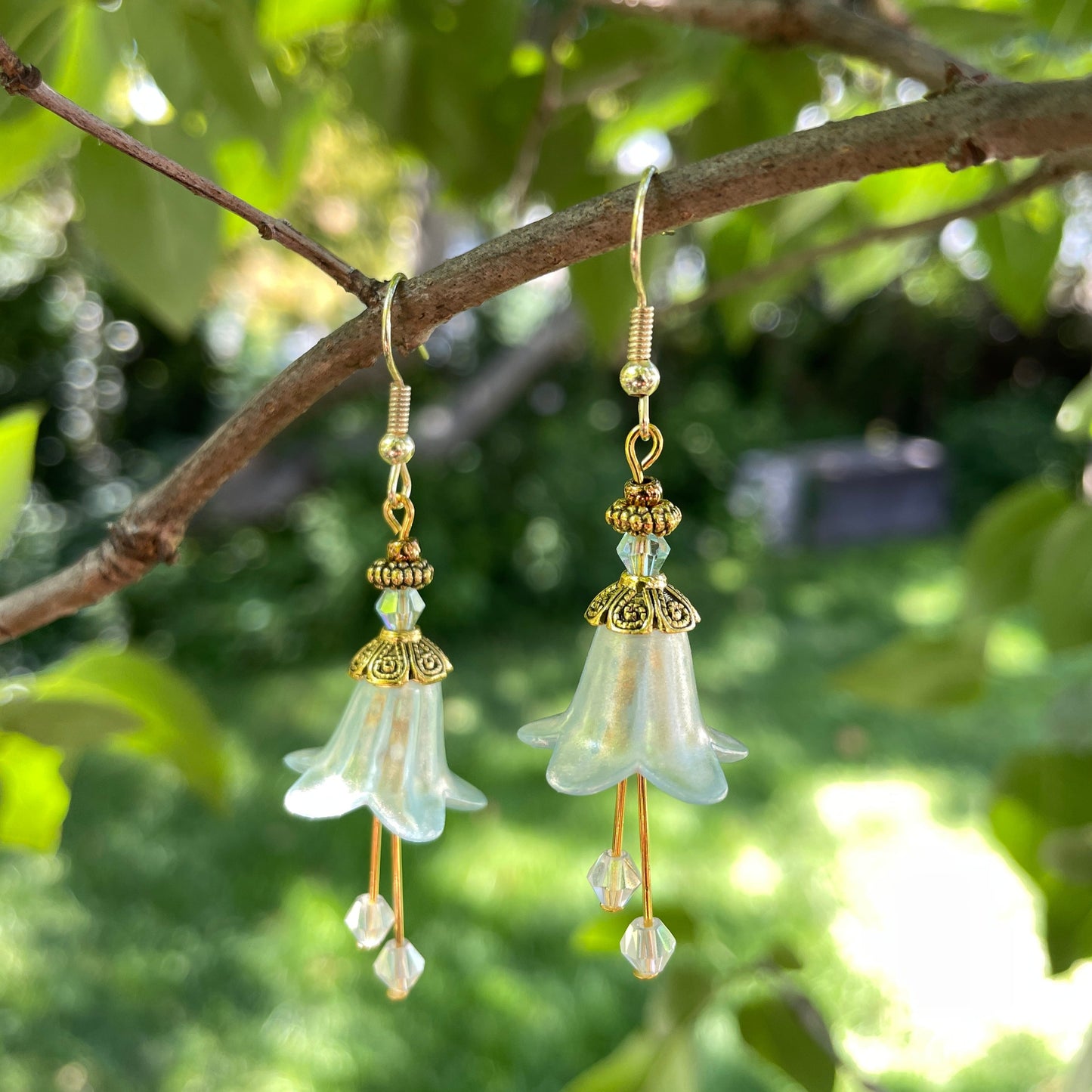 light green bell flower earrings with gold beads and green crystals hanging on a tree branch