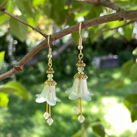 light green bell flower earrings with gold beads and green crystals hanging on a  tree branch