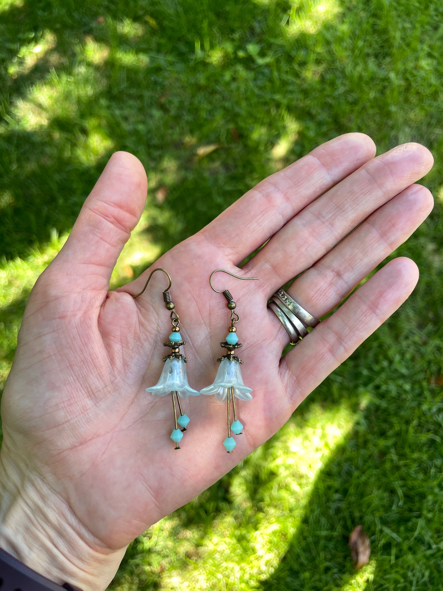 light green bell flowr earings with antique finish held in a hand for size reference.