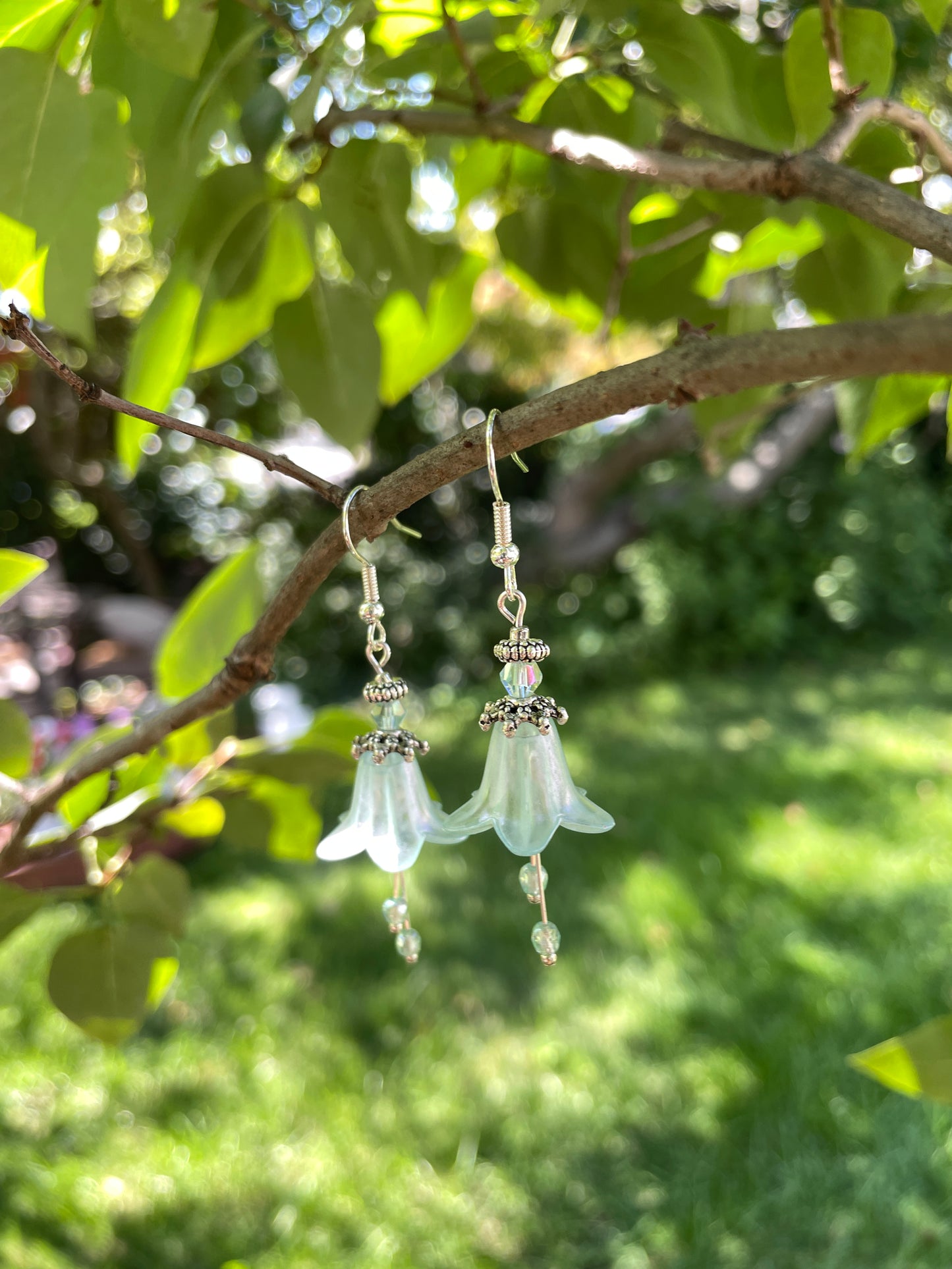 pale green bell flower earrings with silver beads and green crystals hanging from a tree branch.