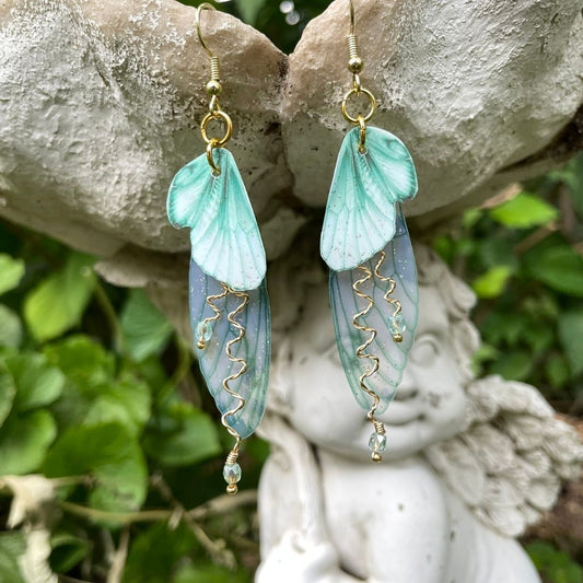 Mint green double wing fairy wings with gold twisted wires with crystals. and gold french ear hooks hanging on a angel garden ornament.