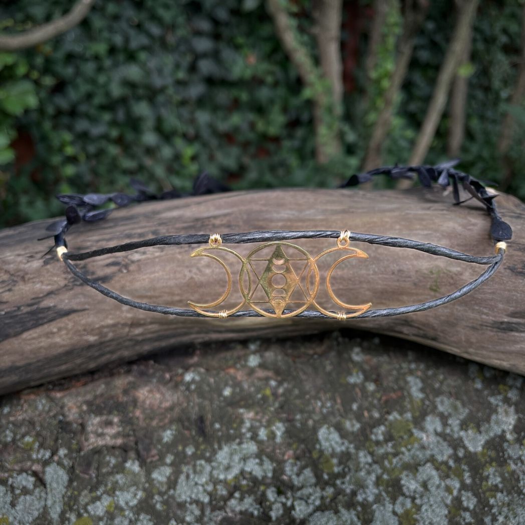 Front view of gold triple moon motif black wired crown sitting on tree branch