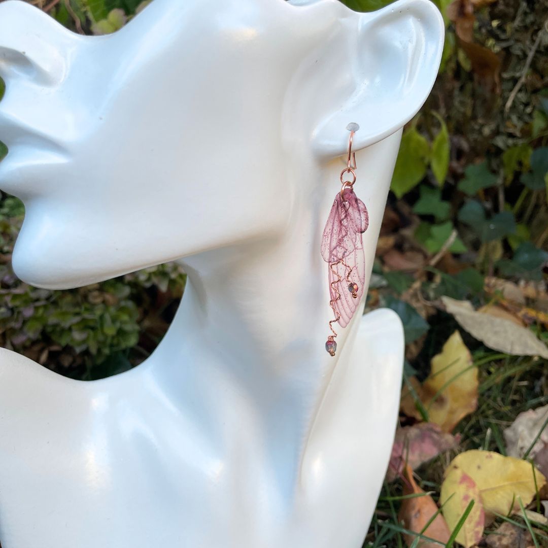 Berry colored fairy wing earrings with crystals displayed on model display