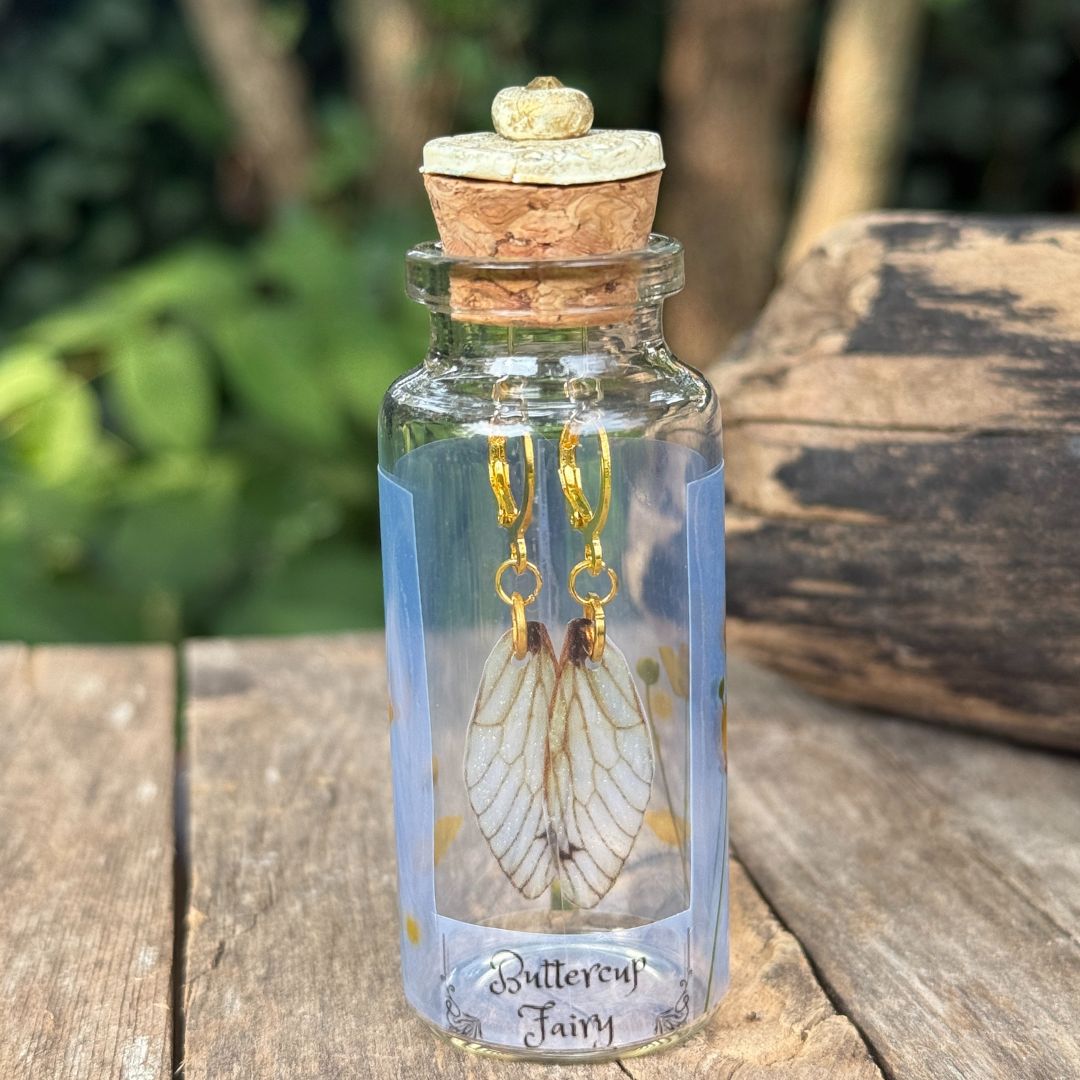 Glass bottle with cork lid containing butterfly-themed earrings on a wooden surface.