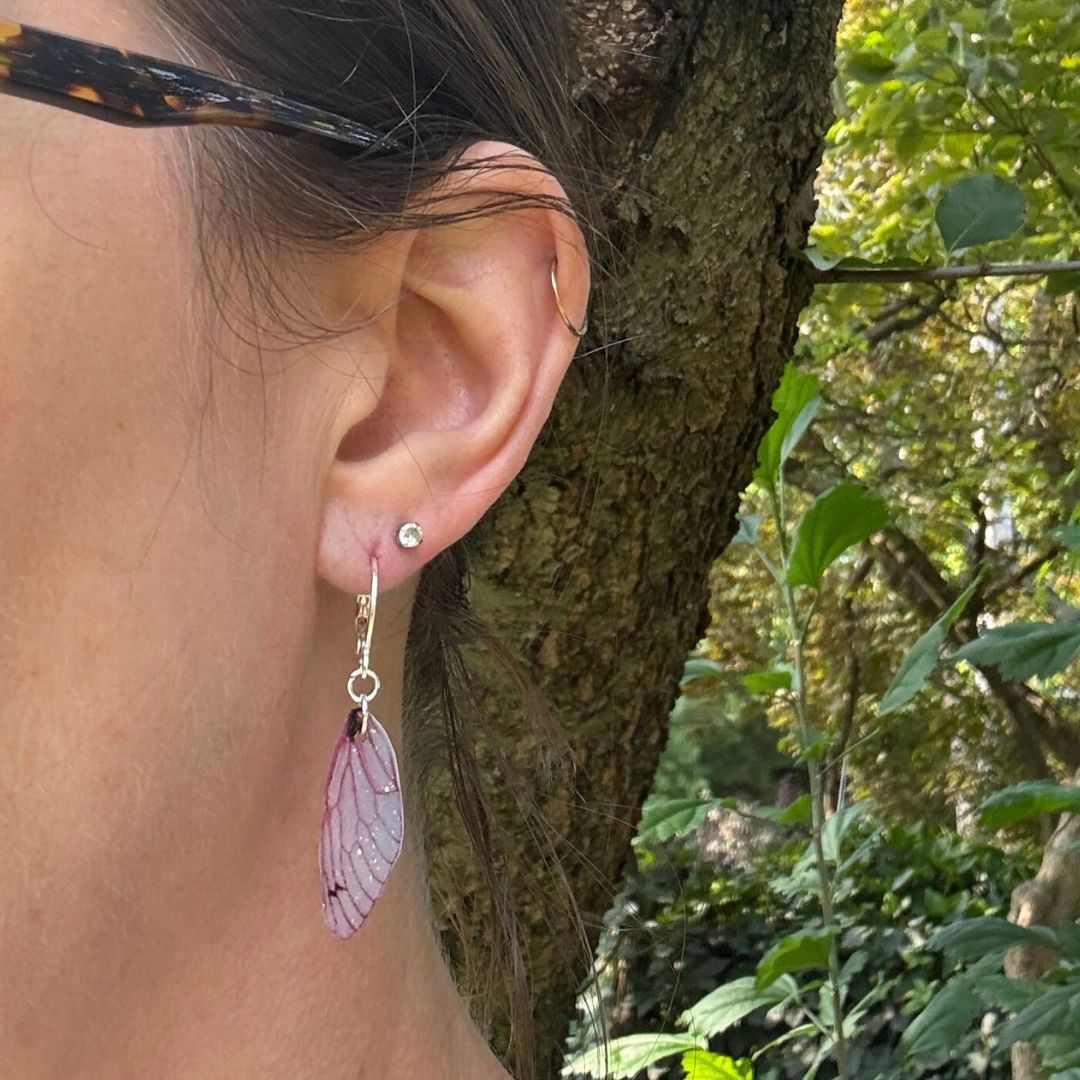 Close-up of an ear with a pink butterfly earring against a natural background