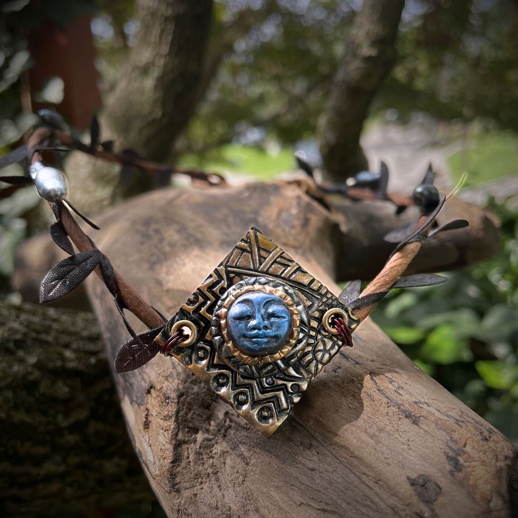 Blue moon on a golden textured diamond shape focal on a brown wire leaf crown resting on a tree branch.