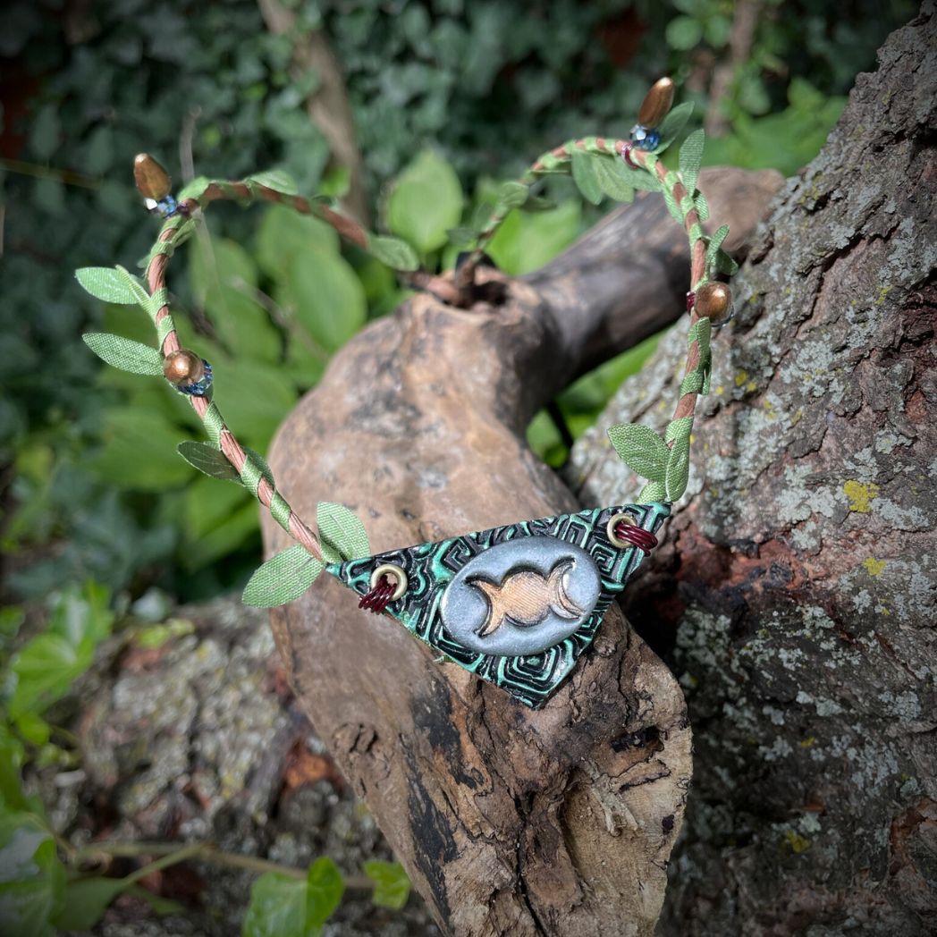 Silver and green triple moon focal on a brown wire and green leaf crown resting on a branch.