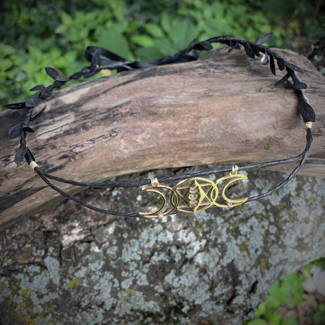 Top view of gold triple moon motif black wired crown with black leaf ribbon placed on tree branch.