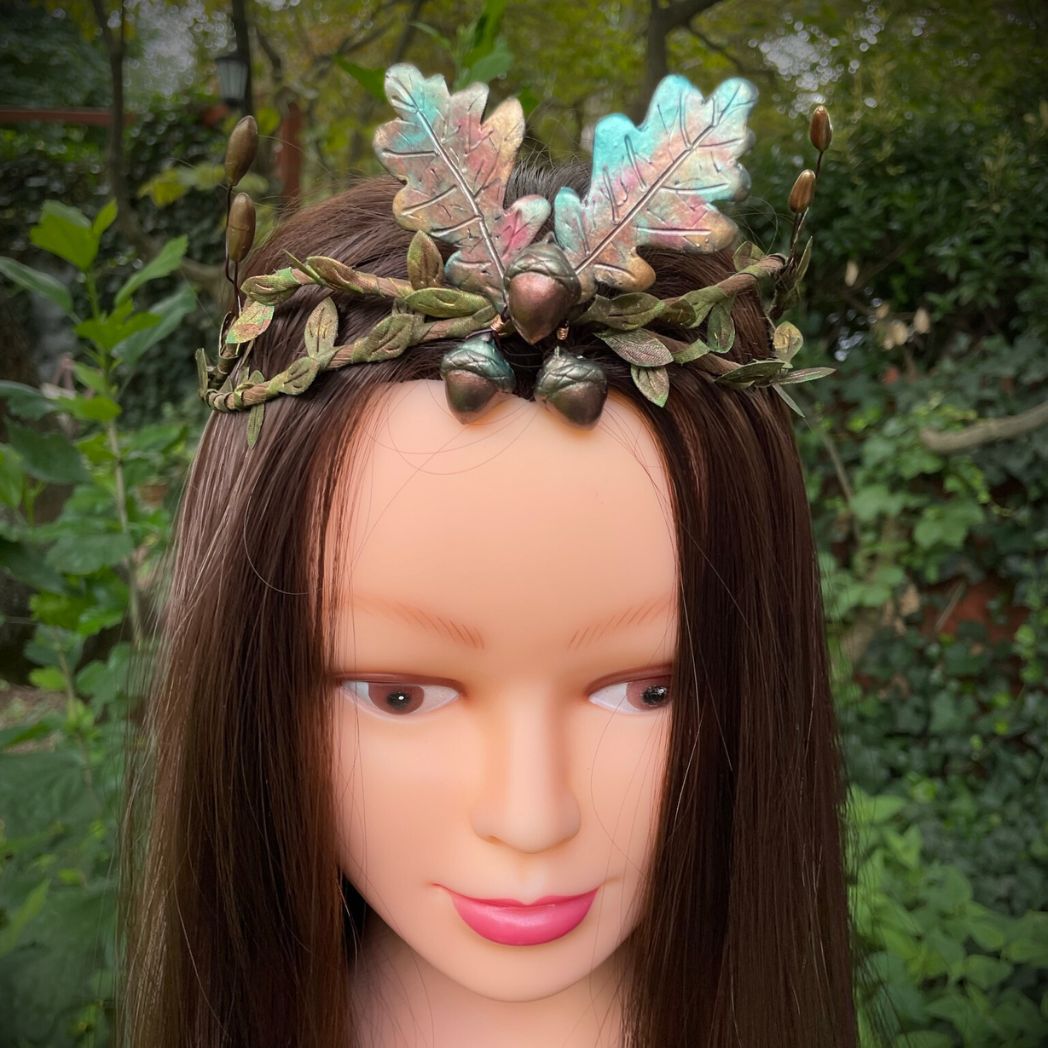 Front fiew  of  a crown with 3 Acorns and 2 oak leaves  in muted Fall colors with green and gold leaf vines and golden buds to the sides.  The crown in displayed on a model